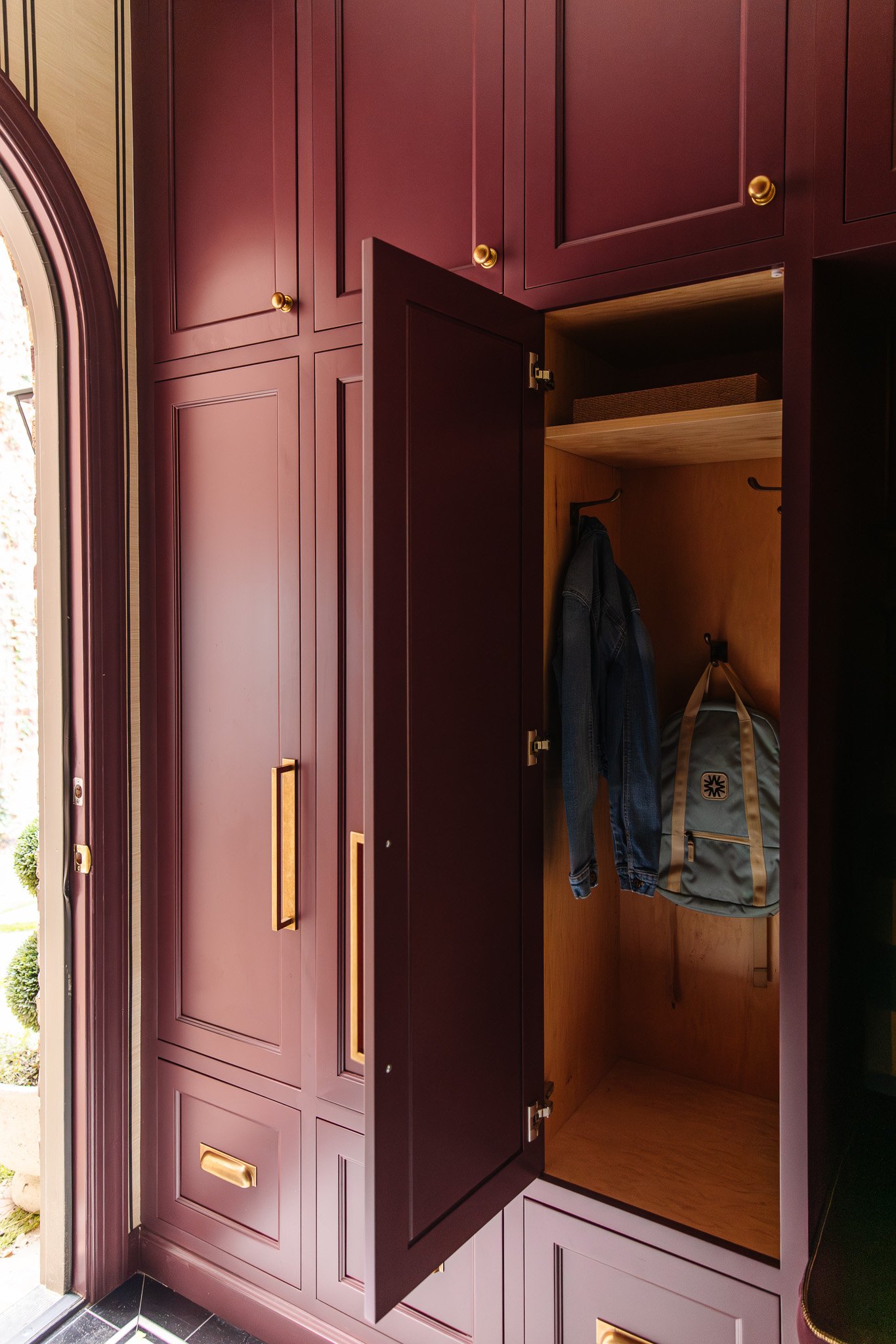 Chris Loves Julia | Moody dark red mudroom with a locker door open to reveal a backpack and denim jacket