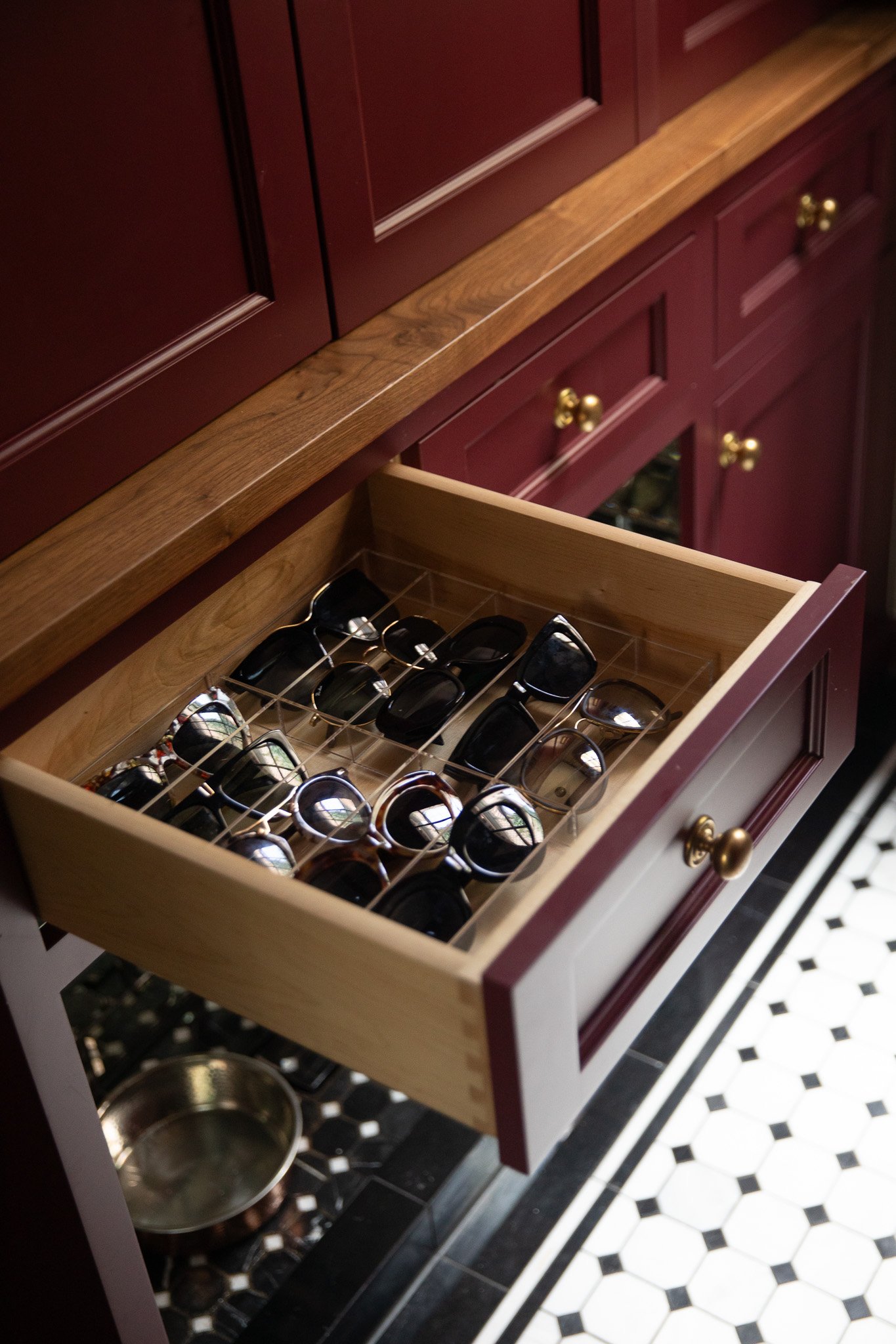 Chris Loves Julia | Moody dark red mudroom with a lower drawer open to reveal sunglasses in trays