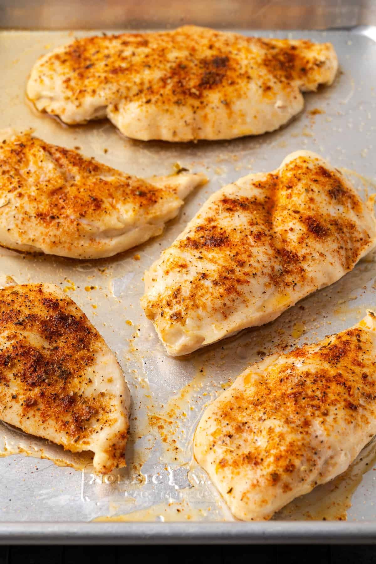 Baked chicken breasts on a metal baking pan.