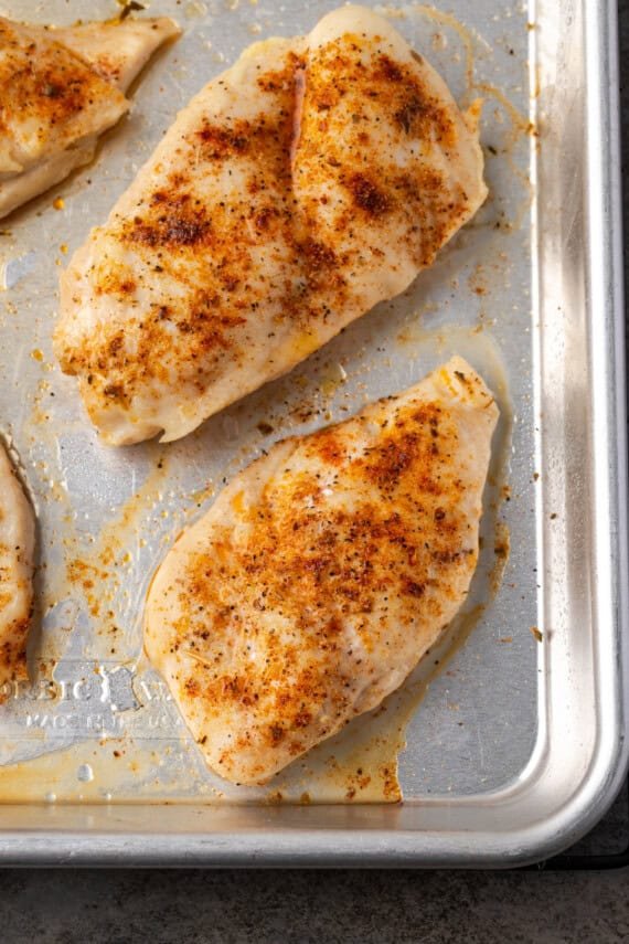 Close up overhead view of baked chicken breasts on a metal baking pan.