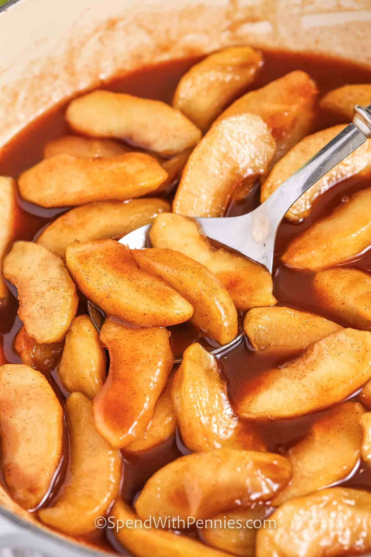 close up of fried apples in brown sugar butter sauce being served from a pan with a spoon