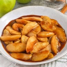 fried apples in a bowl with cinnamon sticks and apples in the background