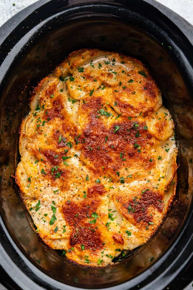 An overhead view of a slow cooker crock full of scalloped potatoes.