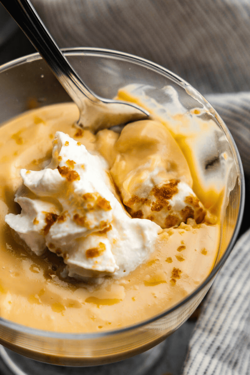 A close up view of a parfait glass of butterscotch pudding with a spoon resting in it having already taken the first bite.